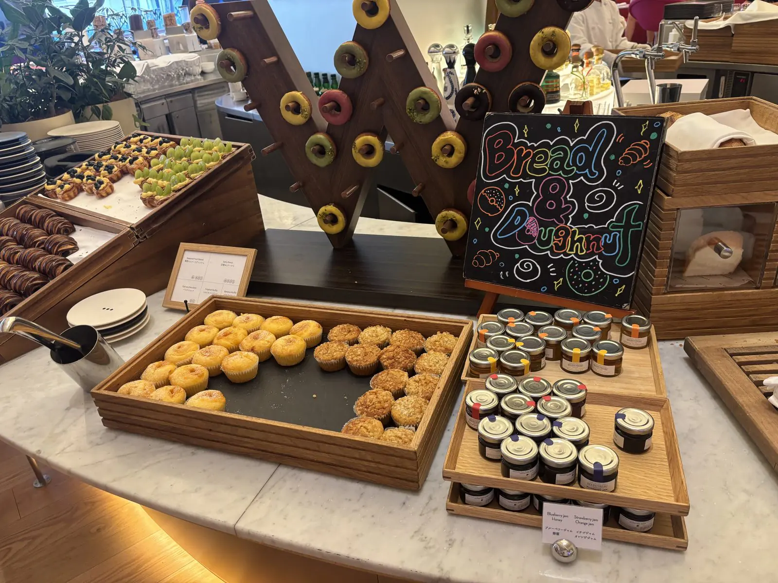 W大阪の朝食ビュッフェのパンコーナー。クロワッサンや焼き菓子、ドーナツが木のトレイに並び、ジャムの小瓶とBread & Breakfastの黒板サインが置かれている