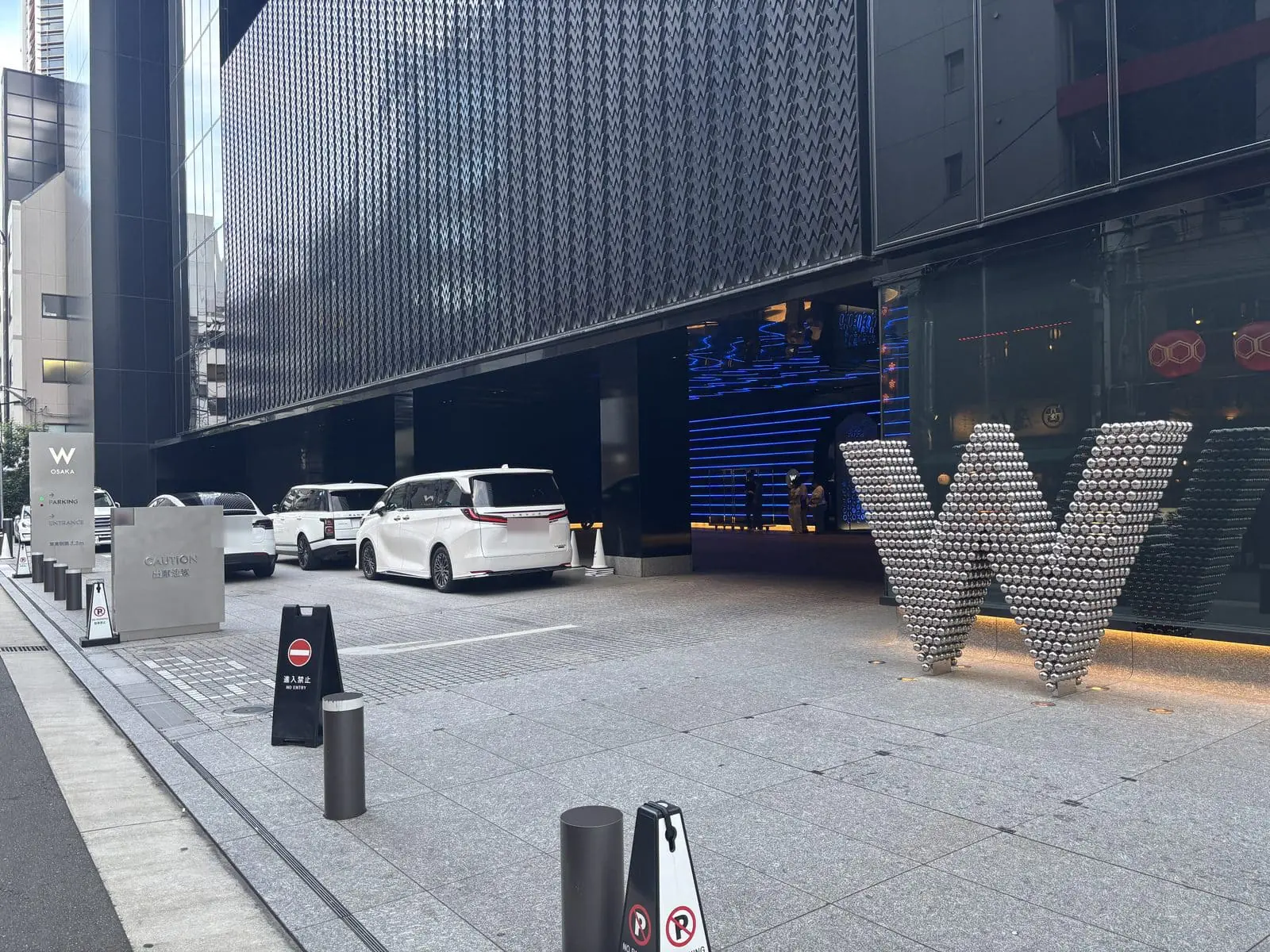 W大阪の車寄せ。歩道沿いにメタリックな立体のWのオブジェが置かれ、奥に車が停まっている