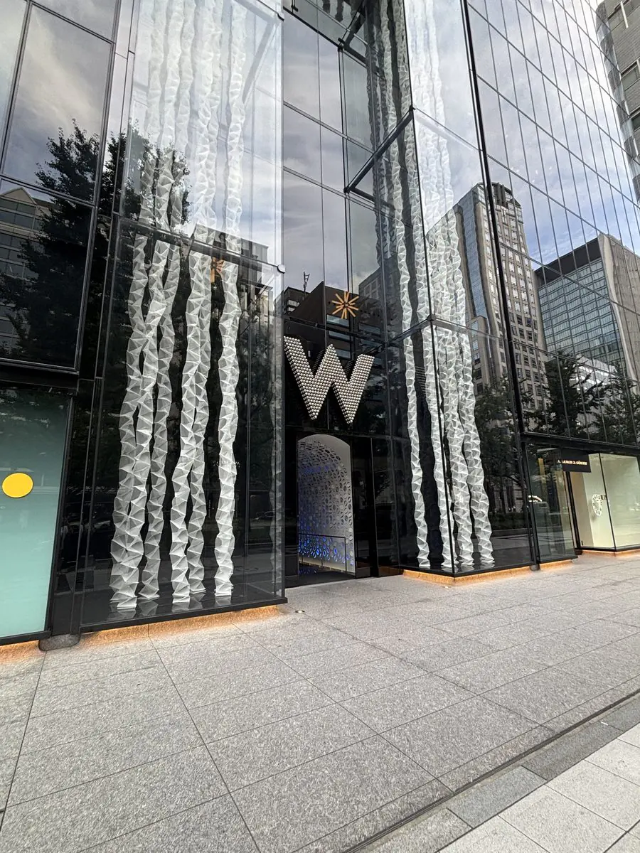 W大阪の外観。黒いガラス張りの高層ビルに白いWのロゴ。手前に水が流れ落ちる壁面がある