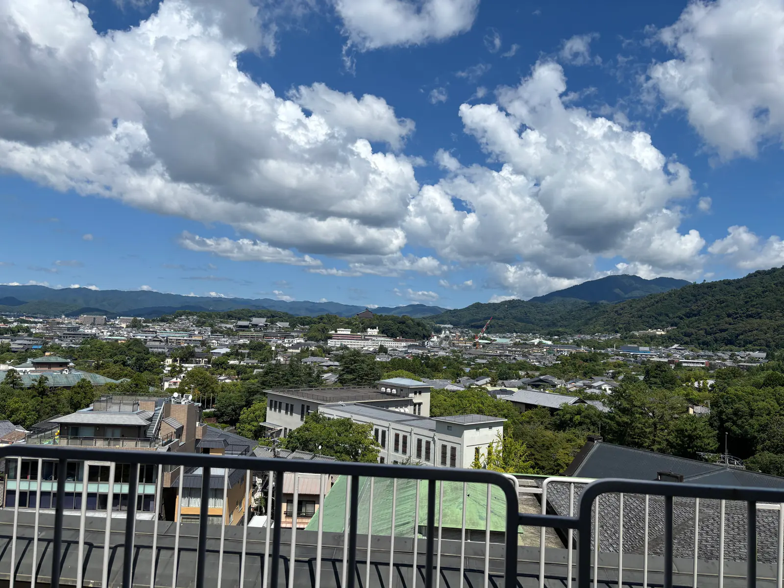 客室のバルコニーの手すり越しに見える京都市街と東山の稜線。青空に大きな雲が浮かんでいる