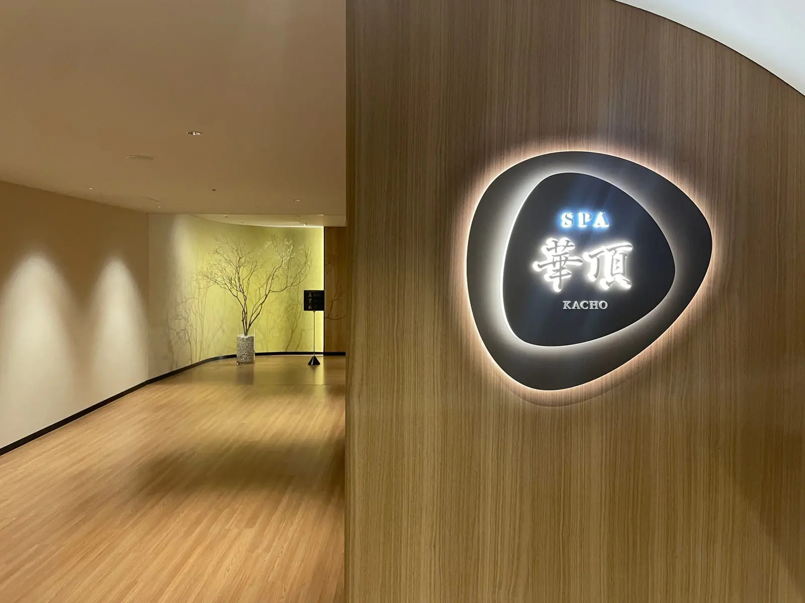 木の壁に埋め込まれた楕円形のサイン。SPA 華頂 KACHO と光る文字で表示されている